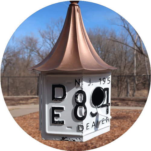 A white license plate made into a bird house with a copper roof.